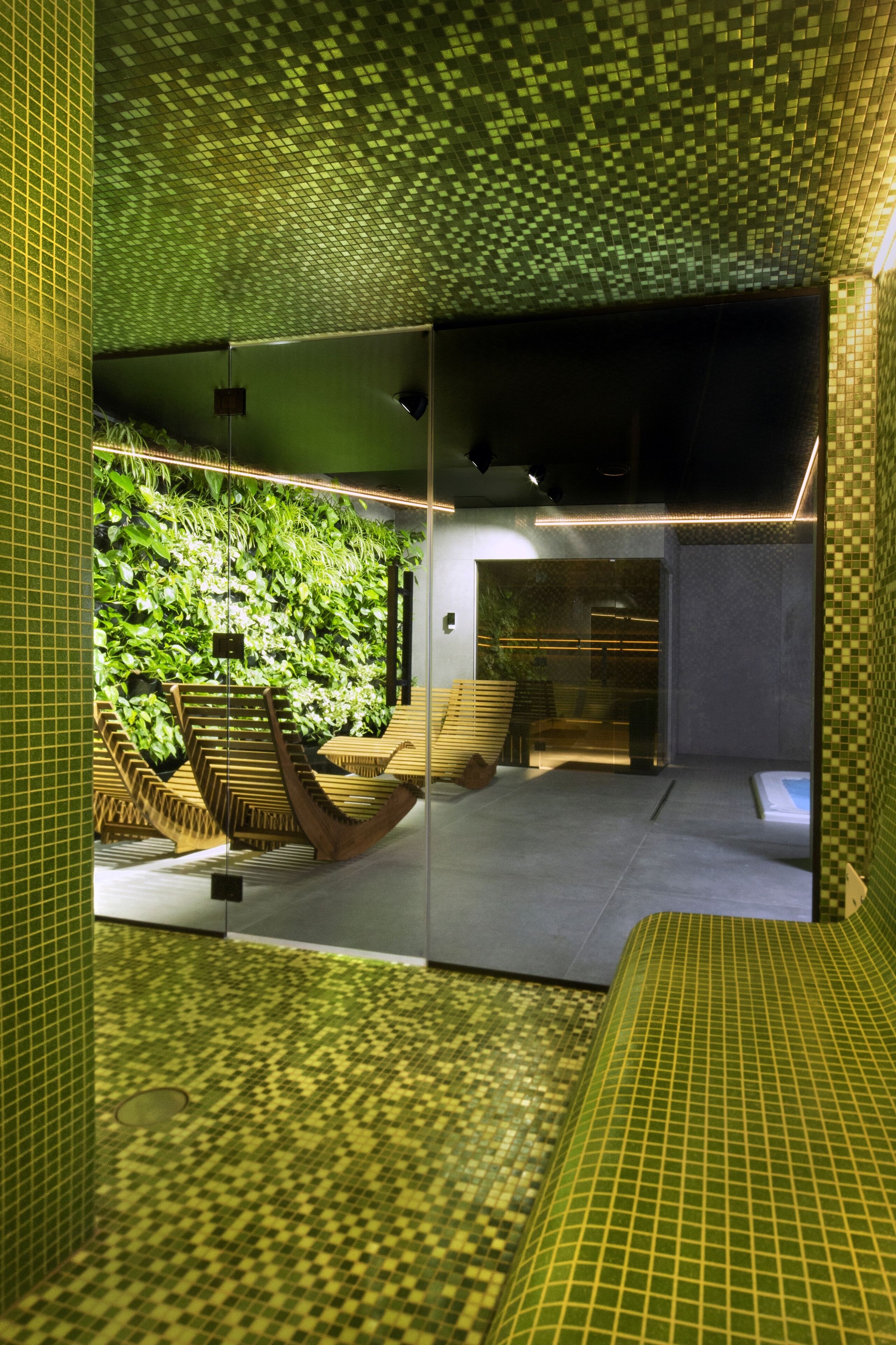 A modern interior with a green-tiled floor, a seating area with a wooden bench, and a wall with a vertical garden.