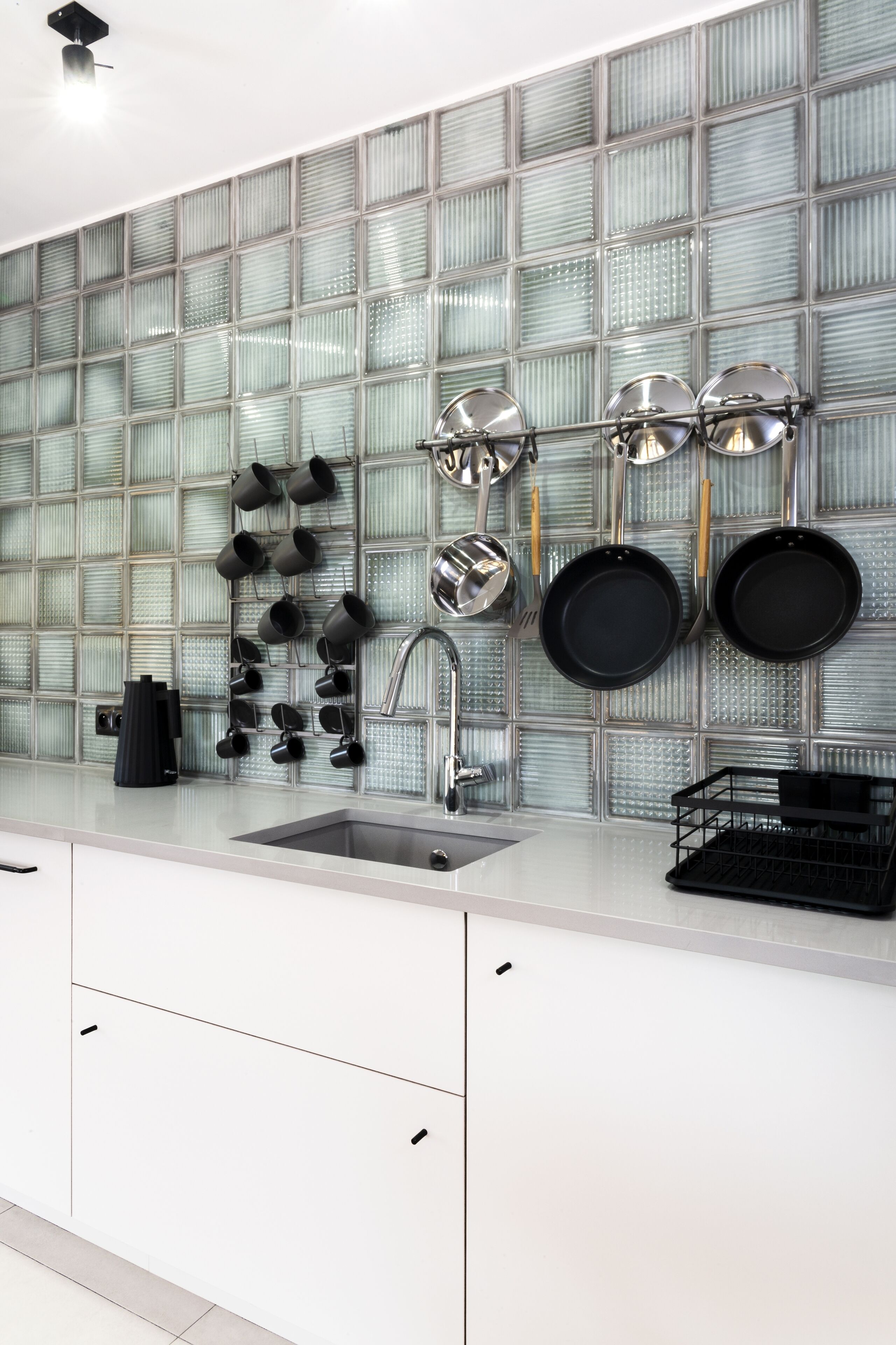 Una cocina de diseño moderno, con un salpicadero de vidrio, un lavamanos de acero inoxidable y una variedad de utensilios y utensilios de cocina colgados en la pared.