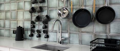 Una cocina de diseño moderno, con un salpicadero de vidrio, un lavamanos de acero inoxidable y una variedad de utensilios y utensilios de cocina colgados en la pared.