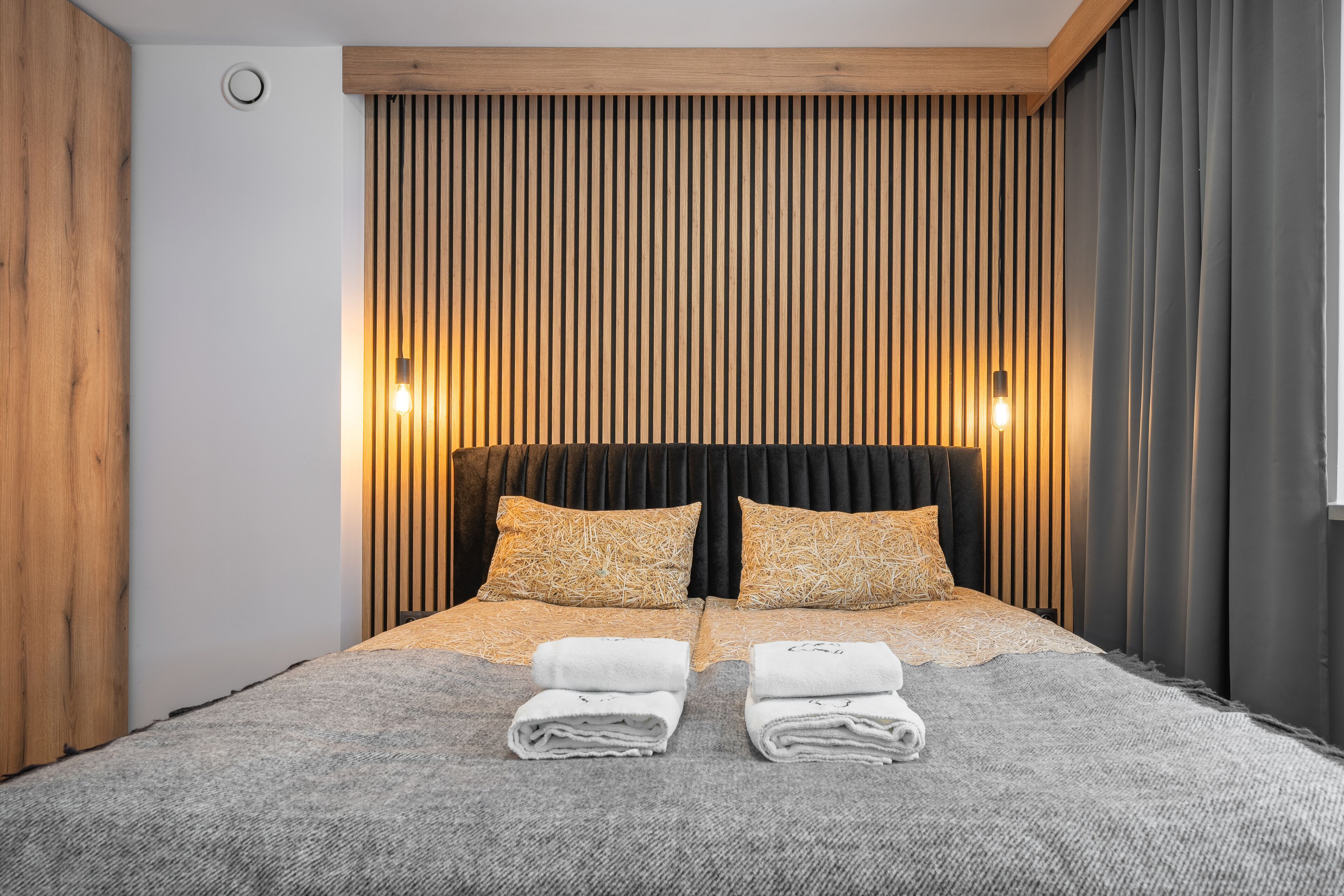Una camera da letto moderna con una testiera in legno a listelli verticali e due lampade da comodino.
