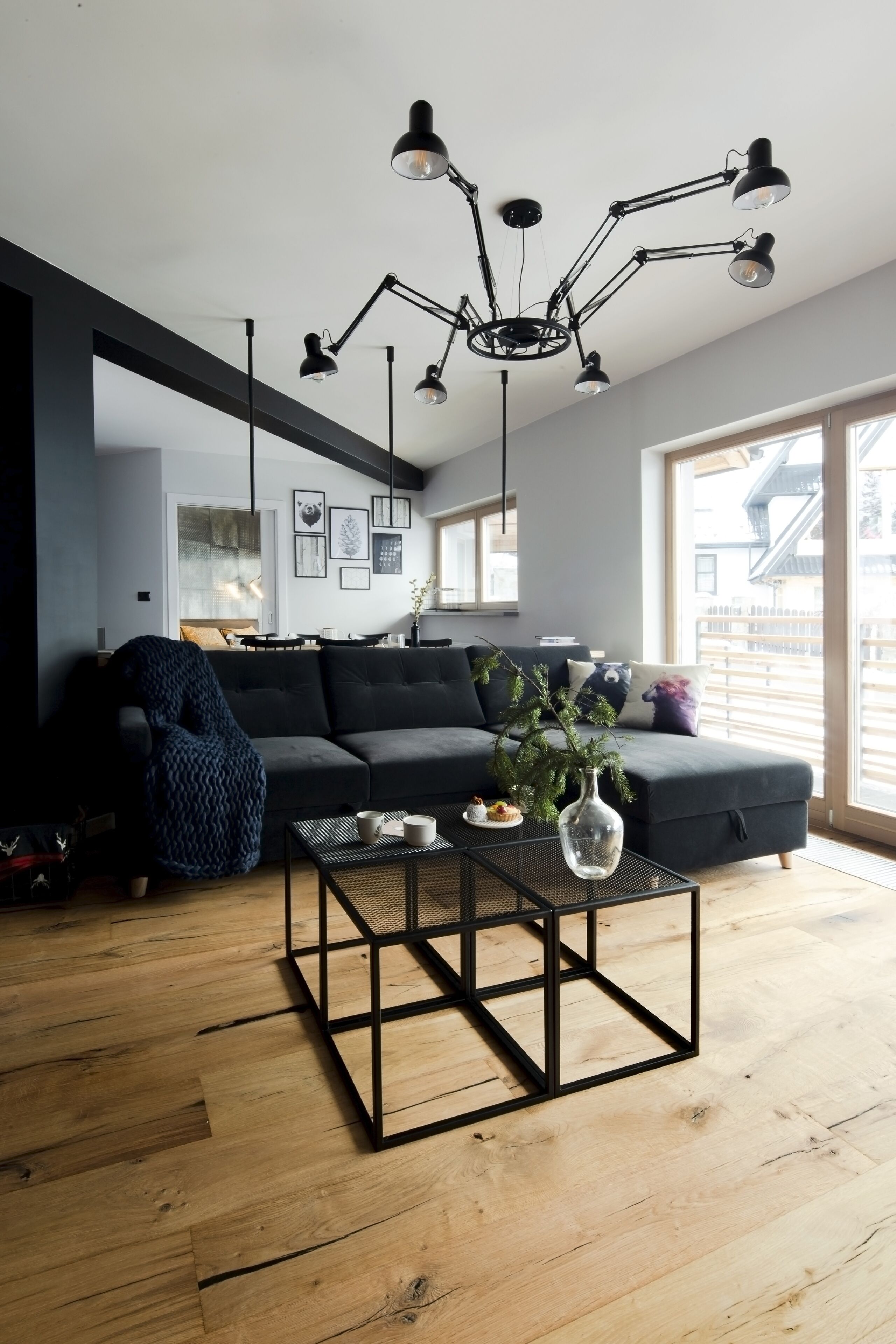 Ein modernes Wohnzimmer mit einem dunkelgrauen Sofa, einem Couchtisch mit einer Vase und einer schwarzen Deckenleuchte.