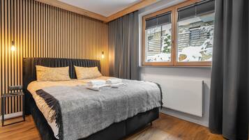 A bedroom with a bed, a bedside table, a window with a view of a snowy landscape, and a wall with vertical wooden slats.