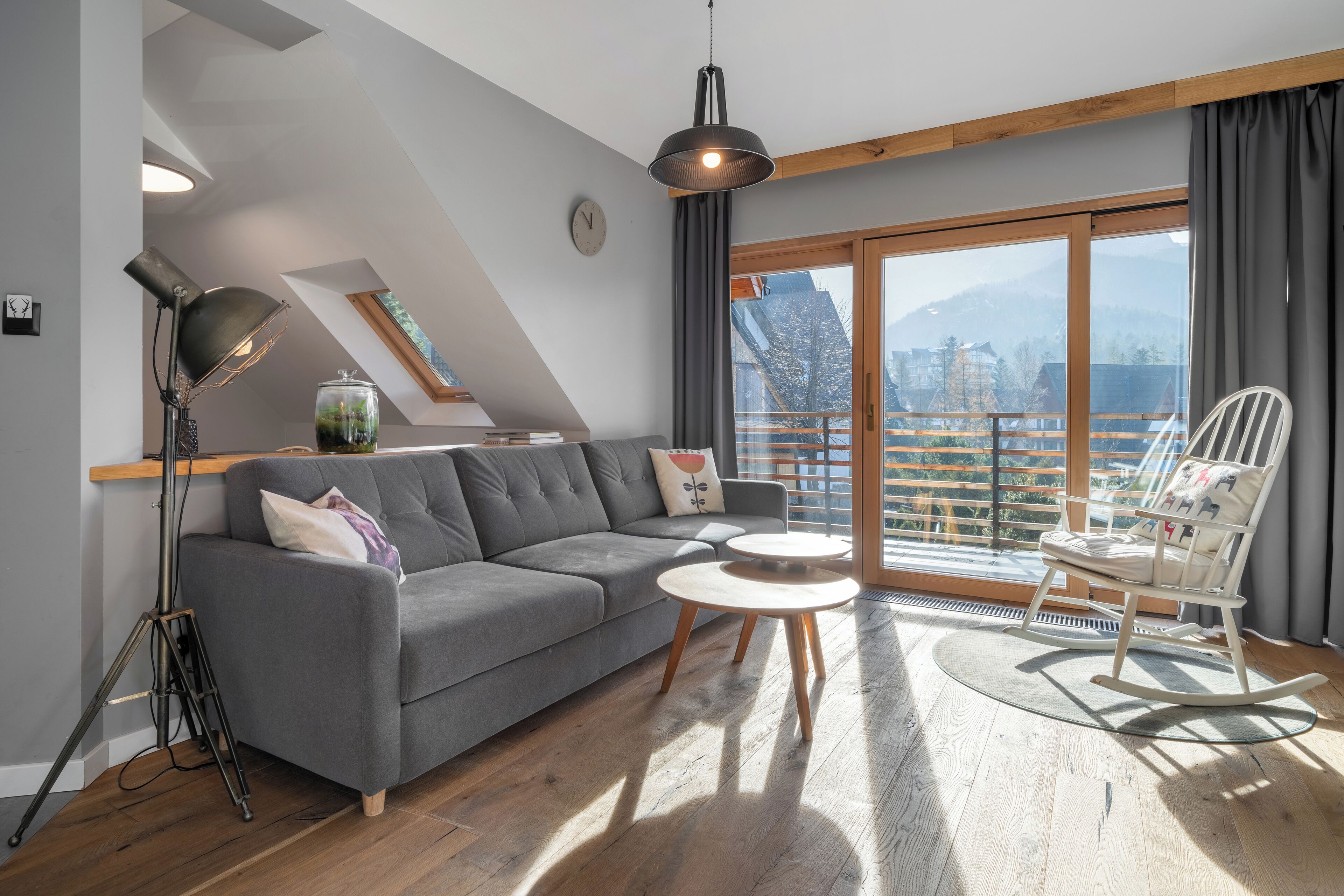 Un salon moderne avec un canapé gris, un fauteuil à bascule blanc, une table basse ronde et un lampadaire.