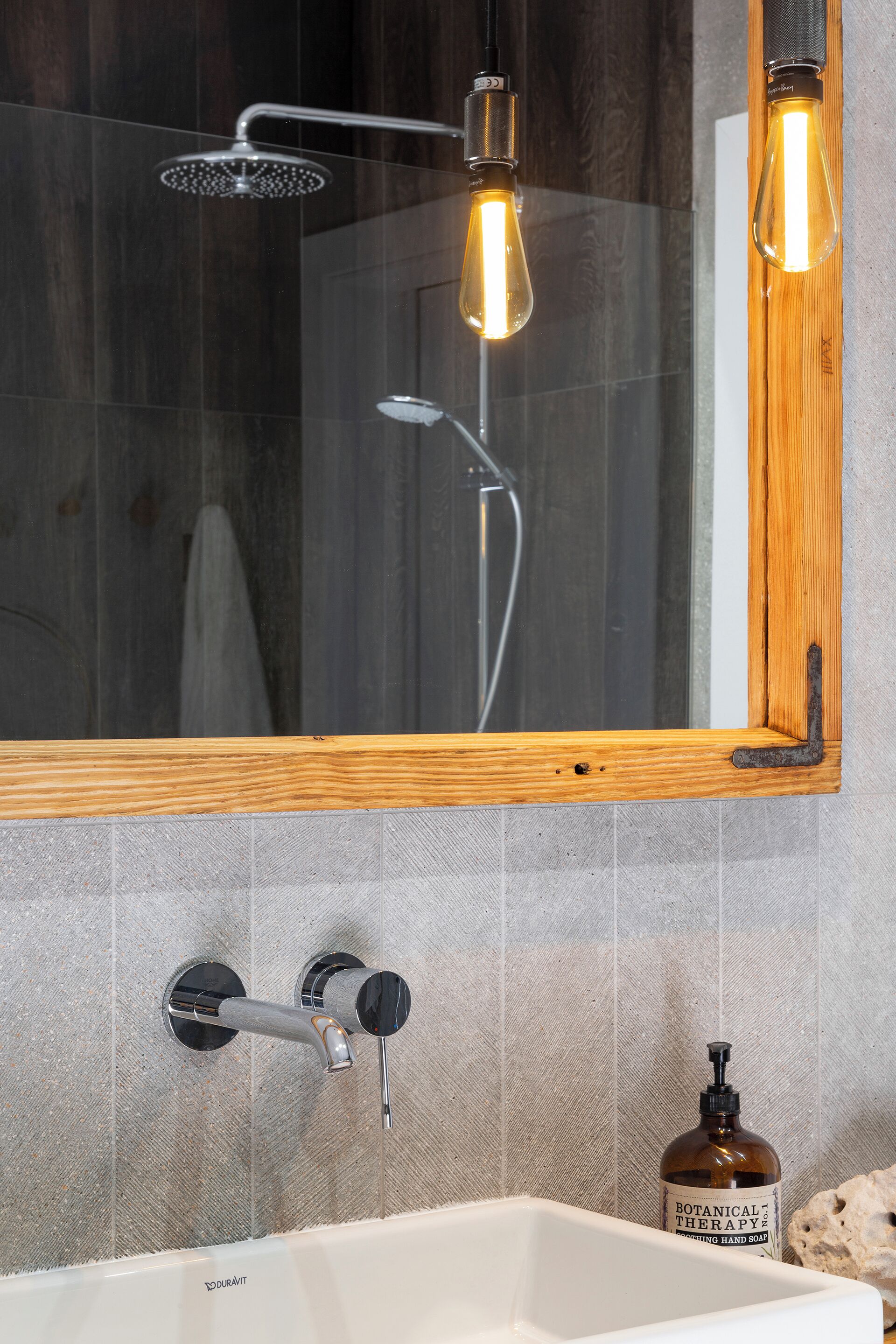 A bathroom with a wooden-framed mirror, a showerhead, and a hand soap dispenser.