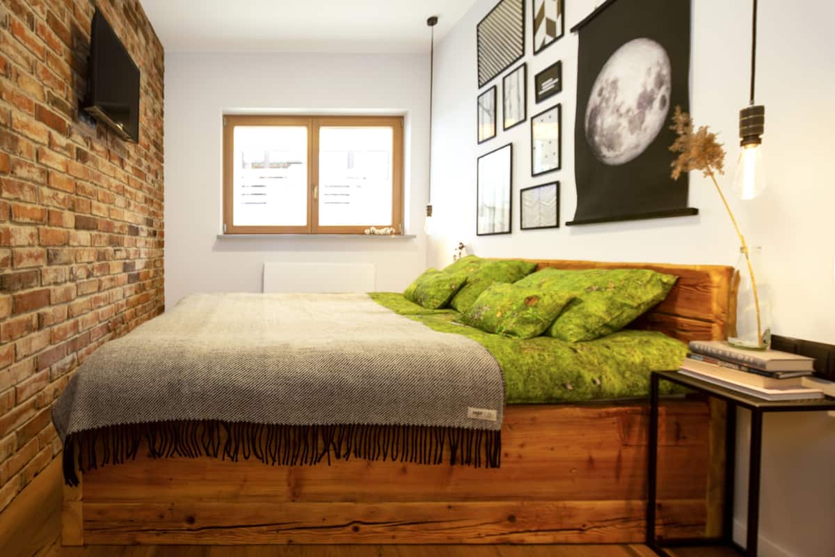 A room with a brick wall, a wooden bed, a window, and a wall with framed pictures.