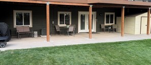 Un espacio cubierto con patio, una zona de estar, una parrilla y un cobertizo pequeño.