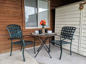 A small outdoor seating area with two chairs and a table, a window with blinds, and a garage door. - Relaxing Retreat with Full Kitchen, King bed, W/D & wildlife (Parker)