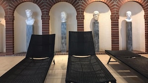 Un espace de détente avec des chaises longues noires et un mur de briques agrémenté de niches en arc abritant des bustes sculptés.