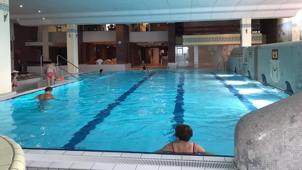 Une piscine intérieure à l’eau d’un bleu limpide, dotée d’une terrasse carrelée et d’un mur en briques orné d’un motif décoratif.