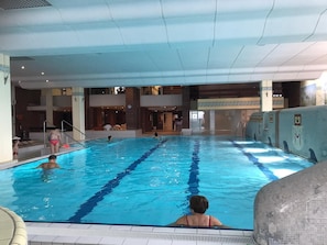 En inomhuspool med kristallklart blått vatten, ett kaklat poolområde och en tegelvägg med ett dekorativt mönster.