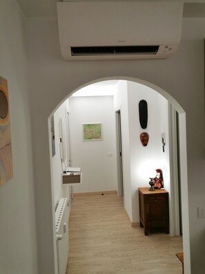 Ein Flur mit Klimaanlage, Holzboden, kleinem Tisch mit Lampe und einer Wandmaske.