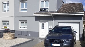 A two-story house with a car parked in the driveway. The house has a tiled roof and a small garden area. - EXCLUSIVE House 100 m2 private parking / garden / 6-8 persons (Liévin)