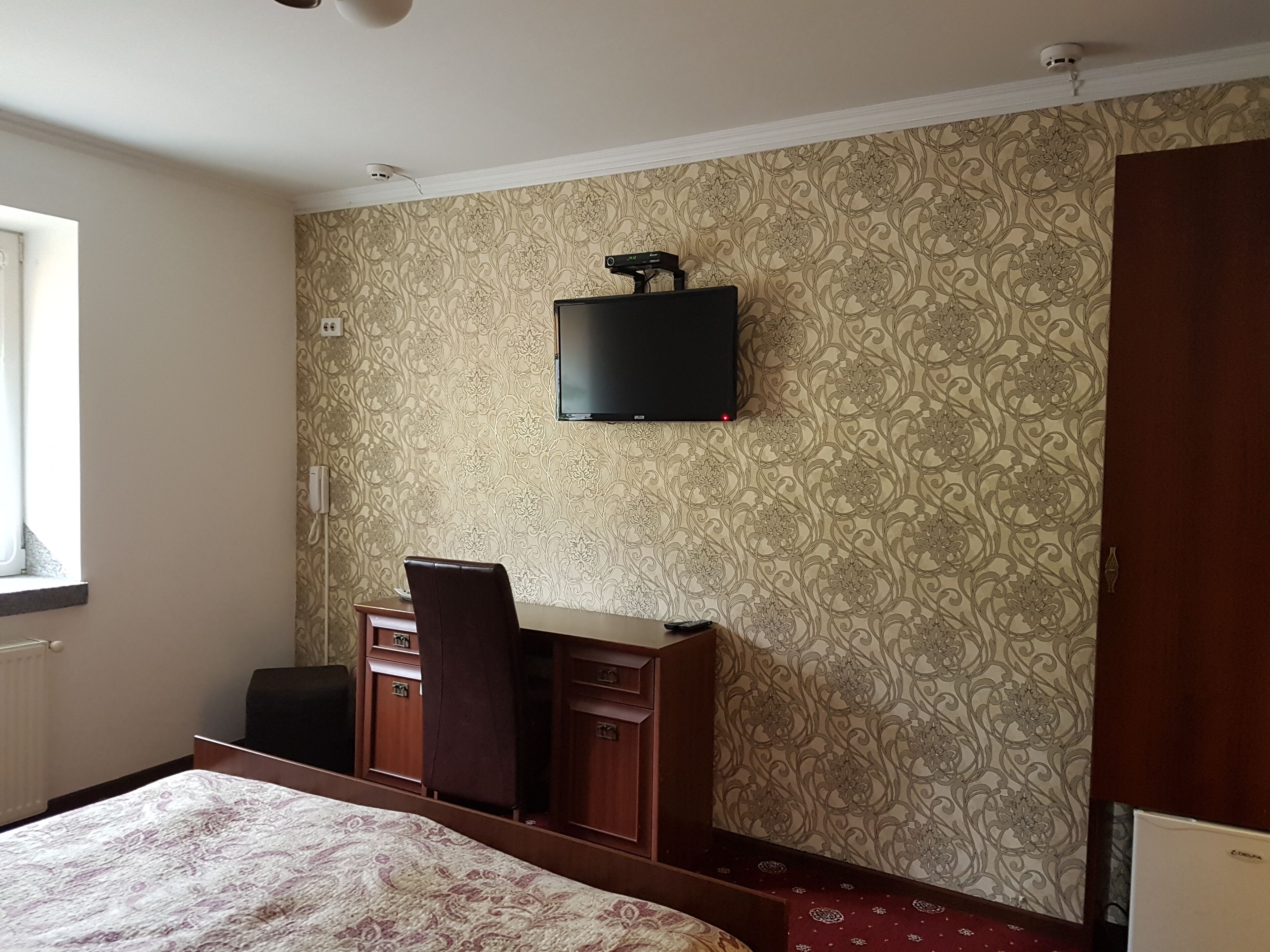 Habitación de hotel con cama, escritorio con silla, televisor montado en la pared y armario.