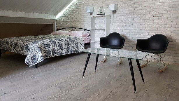 A bedroom with a sloped ceiling, a bed with patterned bedding, a bedside table, two black chairs, and a white brick wall. - Apartments like hotel (Chernivtsi)