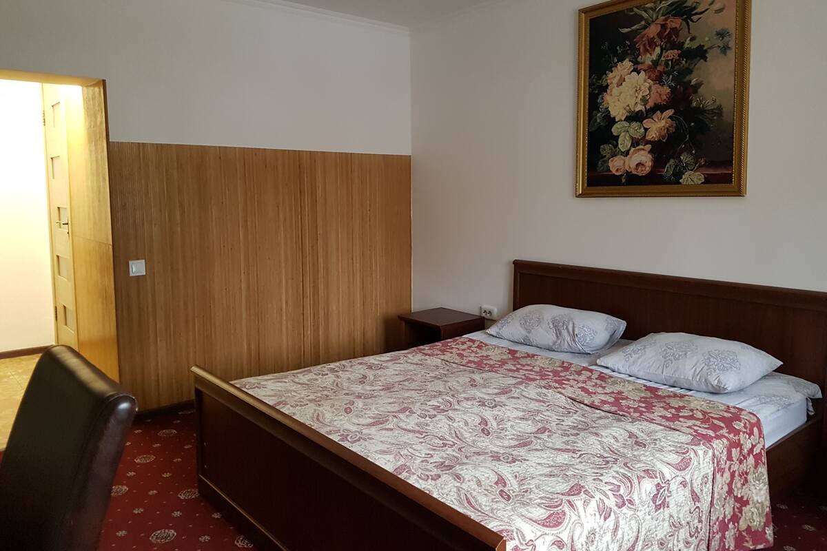 Un dormitorio con un armario de madera, una cama con ropa de cama estampada, una mesita de noche y un cuadro en la pared.