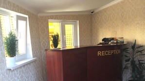 A reception desk labeled "RECEPTION" in a room with patterned wallpaper, a window with a view, and a potted plant. - Apartments like hotel (Chernivtsi)