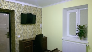 A room with a patterned wallpaper, a mounted television, a desk with a chair, a window with a plant, and a radiator. - Apartments like hotel (Chernivtsi)