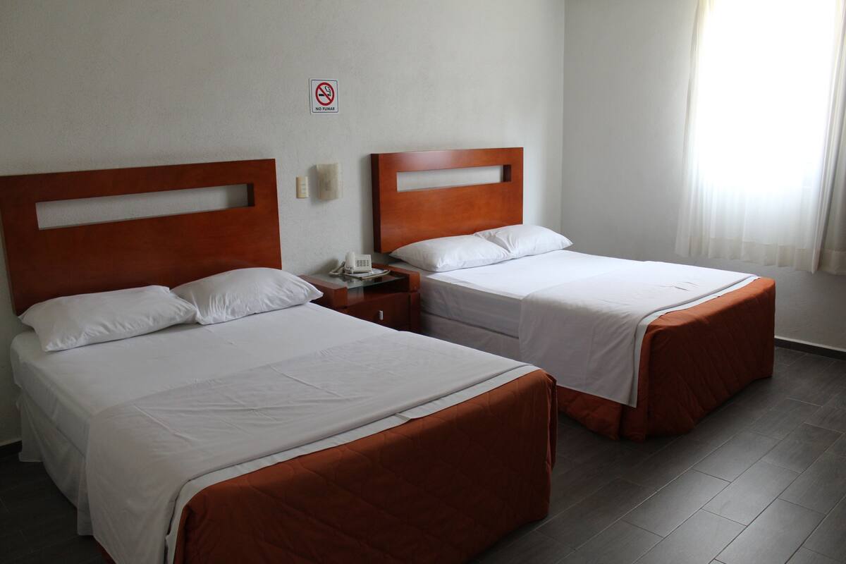 Two single beds with wooden headboards, white bedding, and a no-smoking sign on the wall.