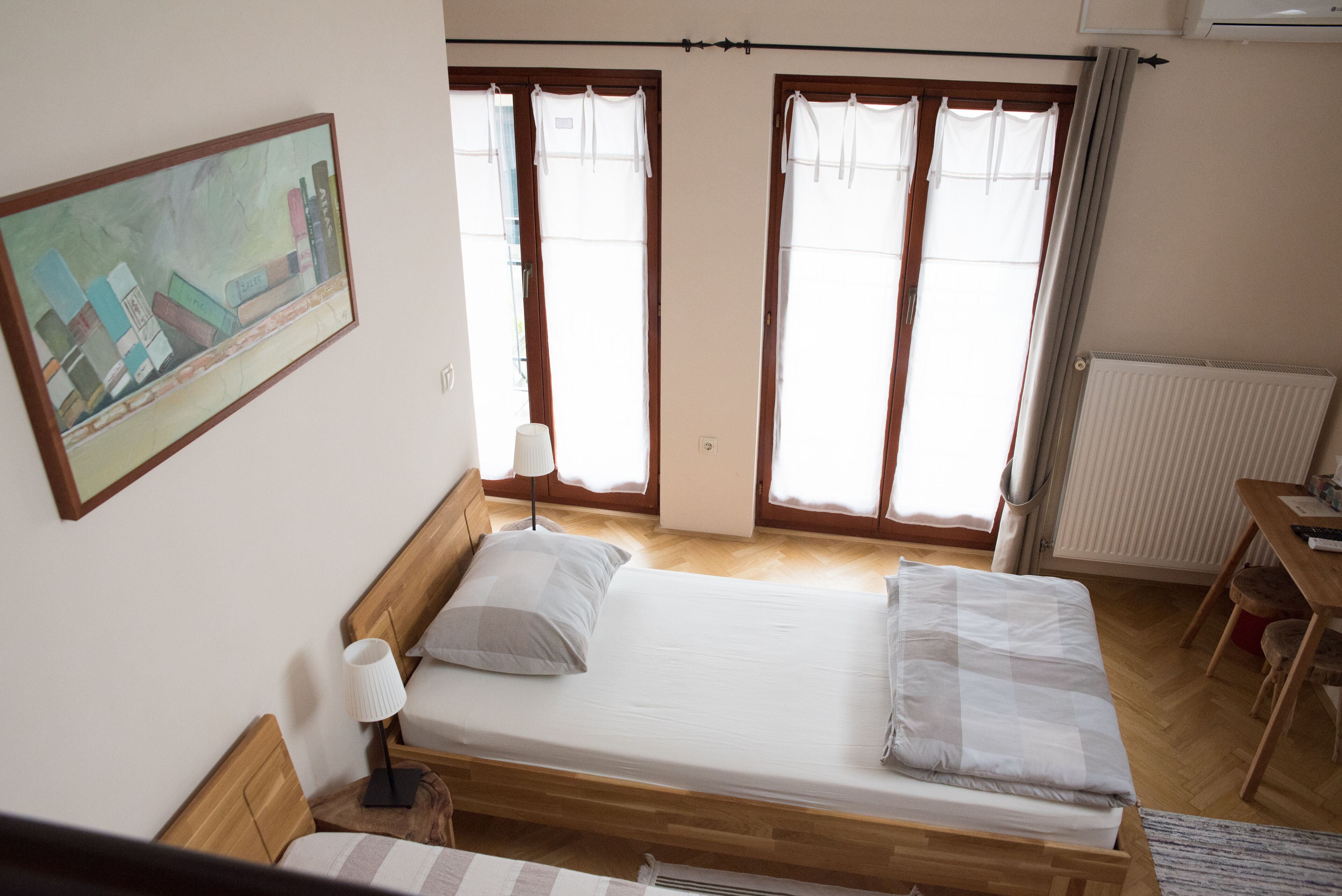 Une chambre à coucher avec un lit en bois, une table de chevet, une lampe, un radiateur et une fenêtre avec des rideaux.