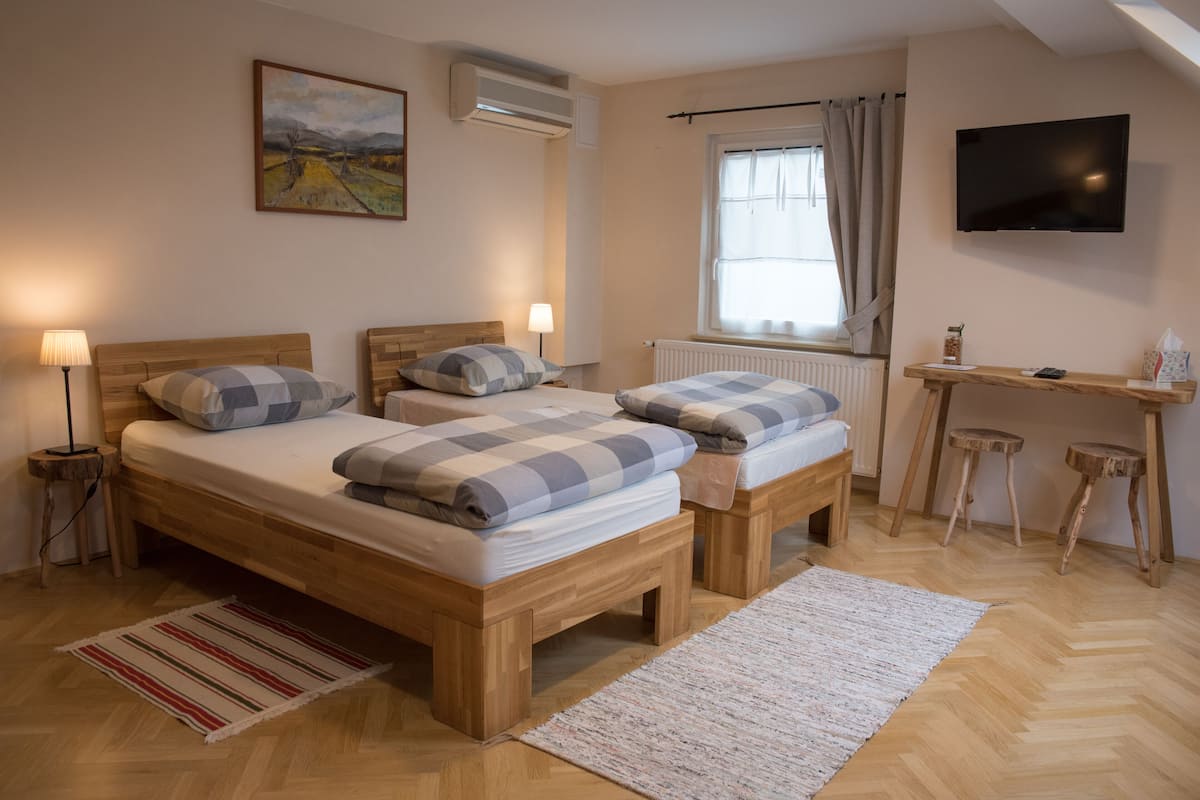 A bedroom with two wooden beds, a TV, a window with curtains, a radiator, and a small desk with stools.