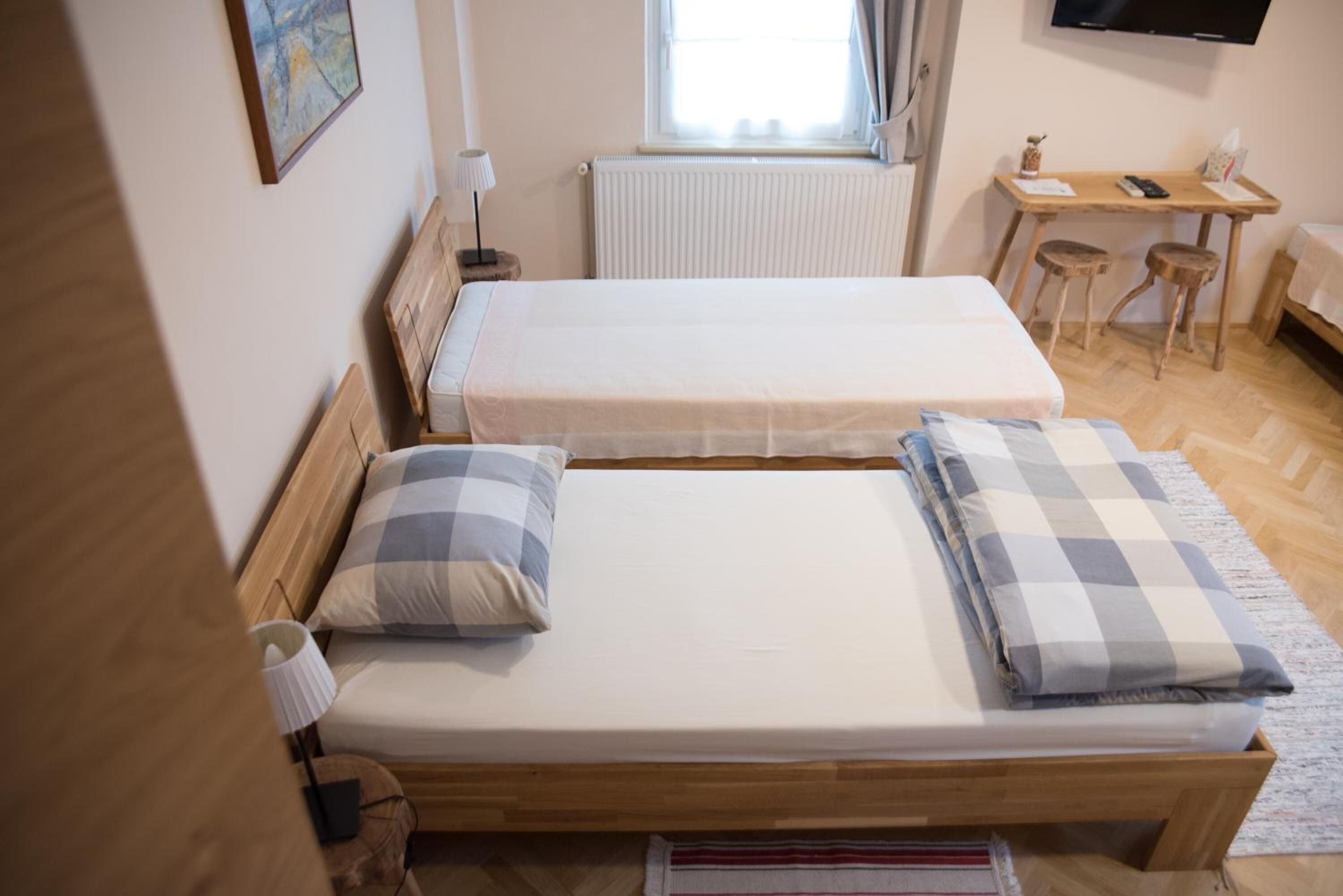 Een kamer met twee eenpersoonsbedden, een houten bureau, een stoel, een radiator en een televisie aan de muur.
