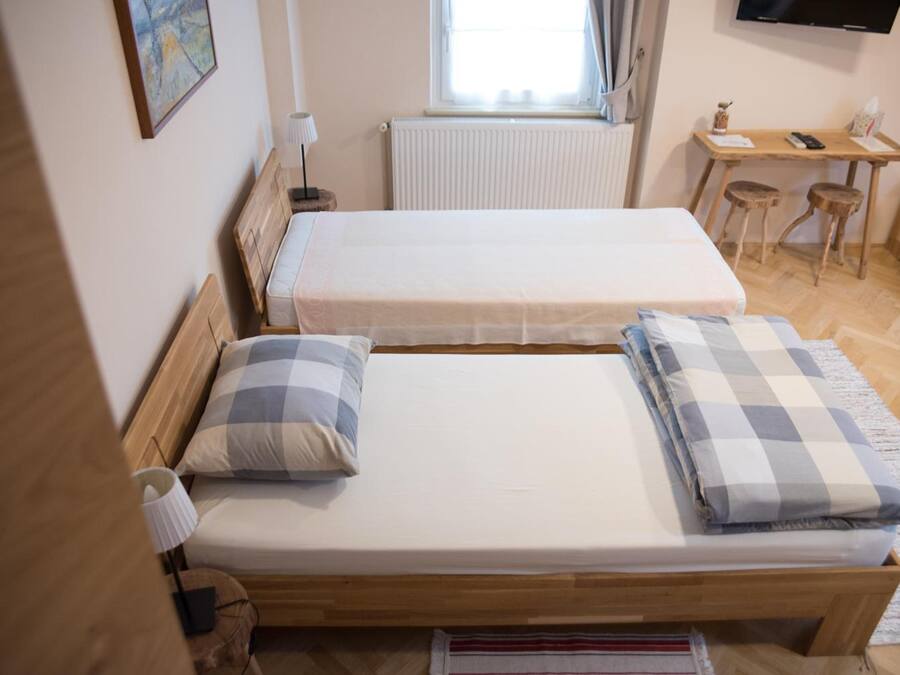 Een kamer met twee eenpersoonsbedden, een houten bureau, een stoel, een radiator en een televisie aan de muur.