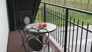 A balcony with a round table and chairs, a small round table with apples, and a view of a green field and distant buildings. - Bed & Breakfast Dvorec (Zalec)
