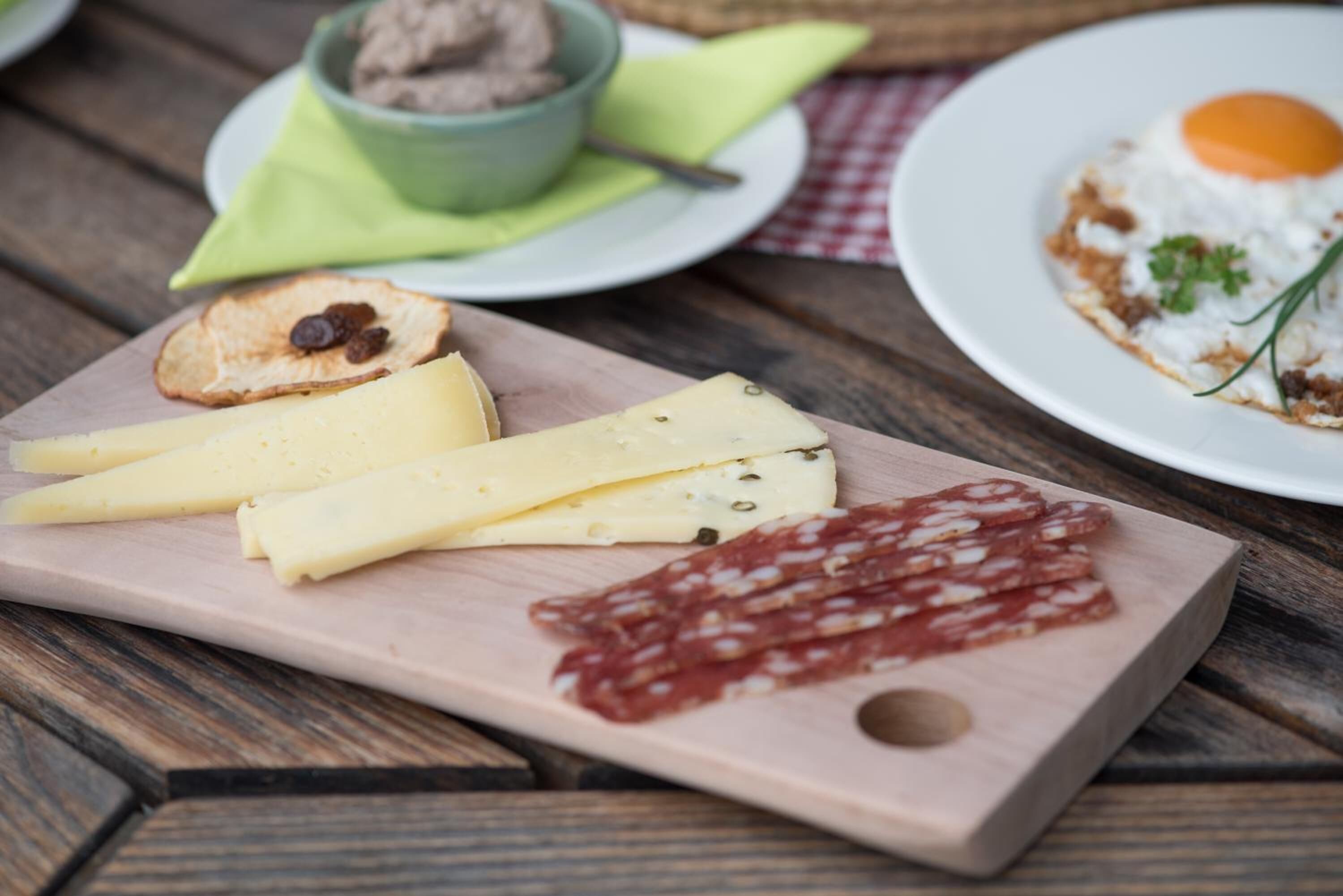 Ein Holzbalken mit Käse, Salami und einer Schüssel Dip auf einem Tisch.