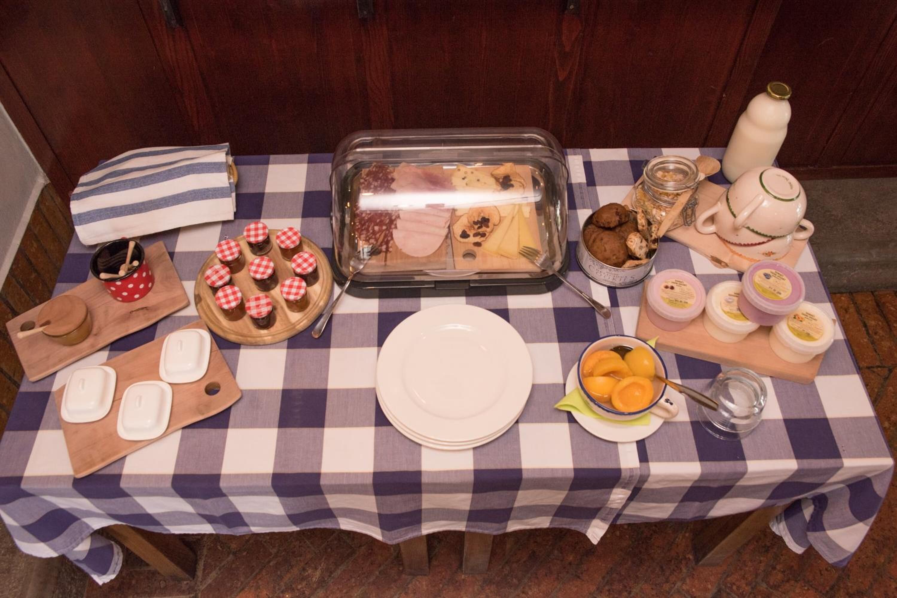 A checkered table with a glass food container, plates, a bowl of fruit, and various food items.