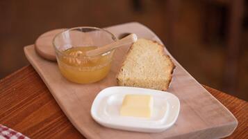 A wooden serving board with a glass bowl of honey, a piece of butter, and a slice of bread.