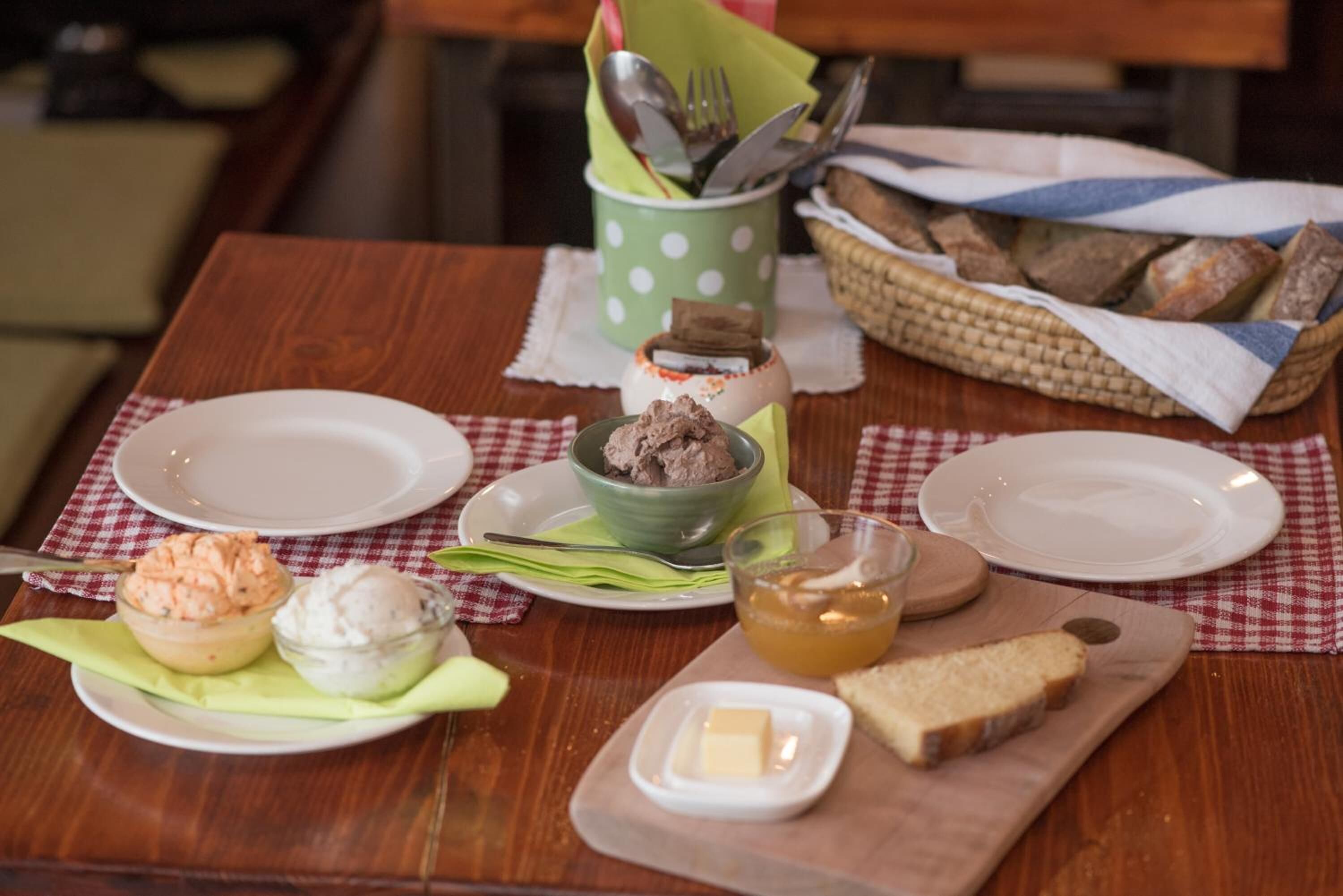 Una mesa de madera con platos, fuentes de comida, una cesta de pan y un portavasos para servilletas.