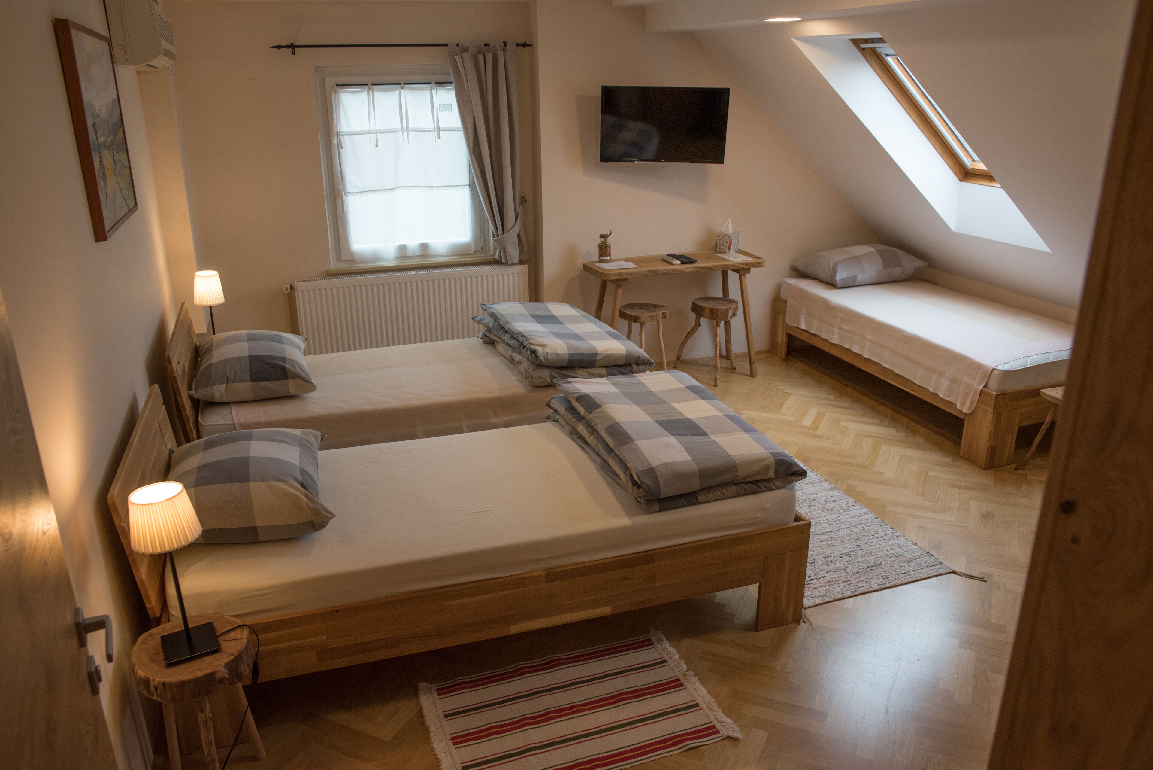 A cozy bedroom with two beds, a desk, a TV, and a window with curtains.