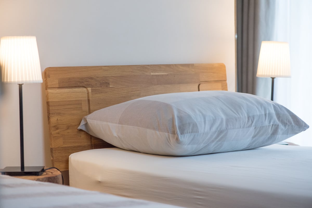 A neatly made bed with a wooden headboard, two bedside lamps, and a bedside table with a lamp.