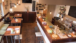 A restaurant with wooden tables and benches, a bar area with a counter and shelves of bottles, and a herringbone floor pattern. - Bed & Breakfast Dvorec (Zalec)