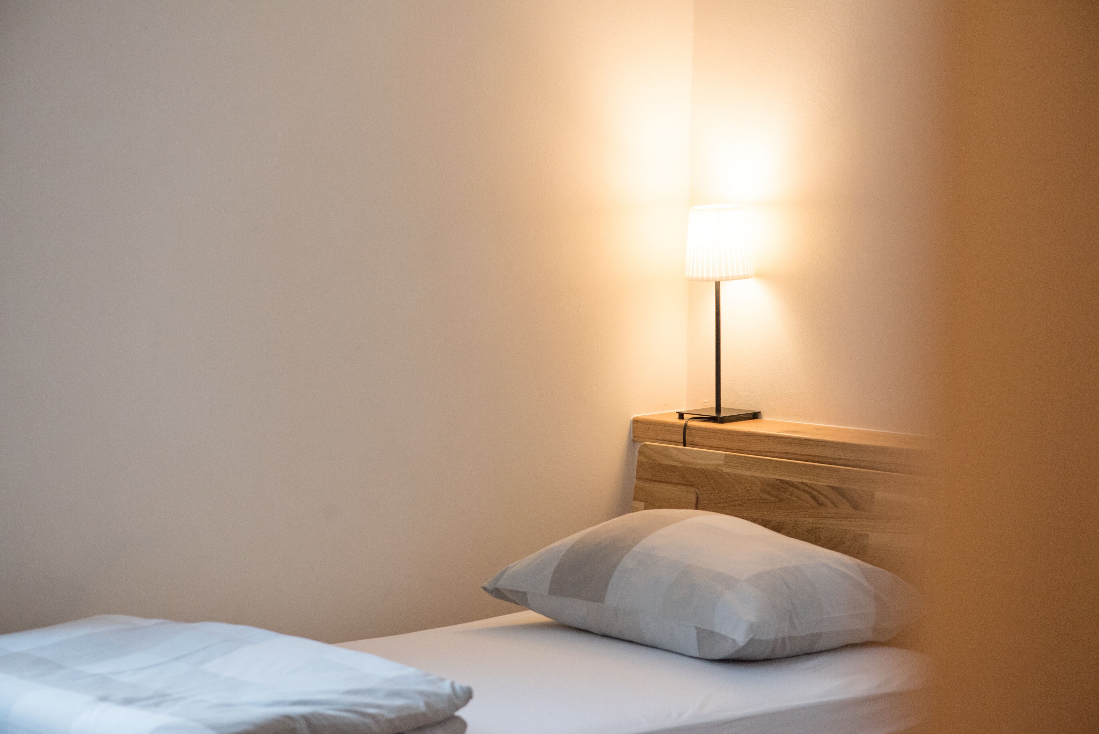 A single bed with a wooden headboard, a bedside lamp, and a pillow.