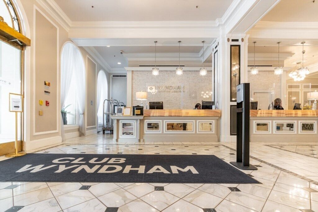 A hotel lobby with a reception desk, a 'CLUB WYNDHAM' mat, and a modern chandelier.