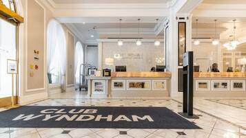 A hotel lobby with a reception desk, a 'CLUB WYNDHAM' mat, and a modern chandelier.
