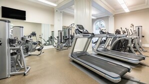 Un gimnasio con cintas de correr, máquinas de pesas y un espejo grande.