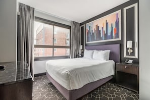 Habitación de hotel con una cama grande, una ventana con cortinas, un cuadro de paisaje urbano y una mesita de noche con una lámpara.