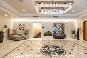 Un vestíbulo con candelabro, suelo de diseño circular, sofá y planta en maceta.
