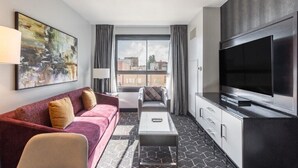Una habitación de hotel moderna con un televisor grande, un sofá, una silla y una mesa de centro.