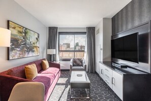 Una habitación de hotel moderna con un televisor grande, un sofá, una silla y una mesa de centro.