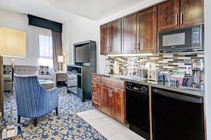 Habitación de hotel compacta con kitchenette, televisor, sofá y alfombra estampada.
