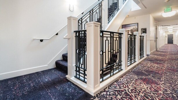 Una imponente escalera con barandales negros y un suelo estampado que conduce a un pasillo.