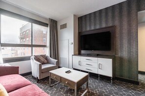 Habitación de hotel con una ventana grande, televisor de pantalla plana, sofá, mesa de centro y un armario.