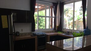 A kitchen with a gas stove, refrigerator, and a window with curtains. - Tropical, private, safe brand new 3 bedroom home (panajachel)