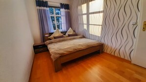 Une chambre à coucher avec un lit en bois, une table de chevet, une commode et une fenêtre avec des rideaux.