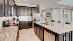 A modern kitchen with dark cabinetry, stainless steel appliances, and a granite countertop. - 5 STAR Luxury Home, Indoor Playground, Baby Friendly, Solara Resort, Near Disney (Kissimmee)