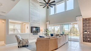 A spacious living room with a large sectional sofa, a patterned armchair, a ceiling fan, and a TV. - 5 STAR Luxury Home, Indoor Playground, Baby Friendly, Solara Resort, Near Disney (Kissimmee)
