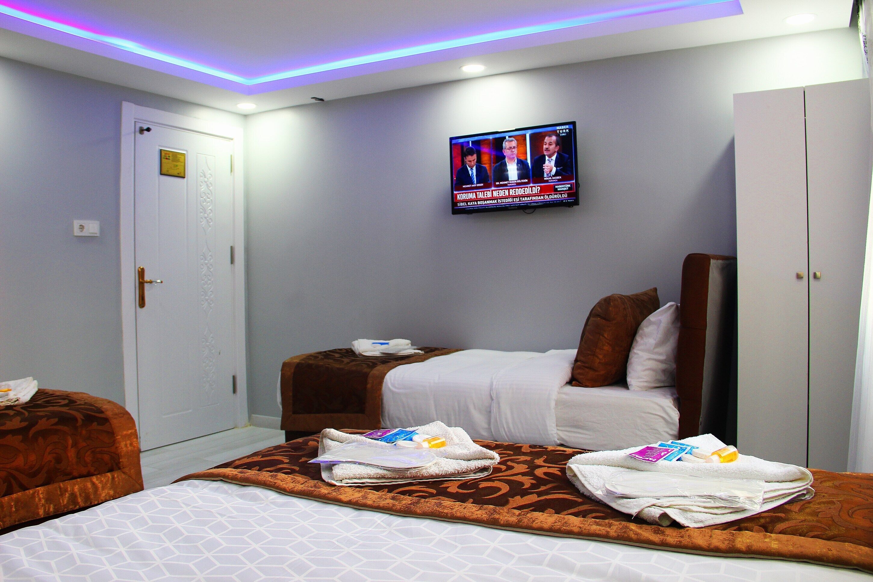Hotellihuone, jossa on kaksi sänkyä, seinälle asennettu televisio ja vaatekaappi.